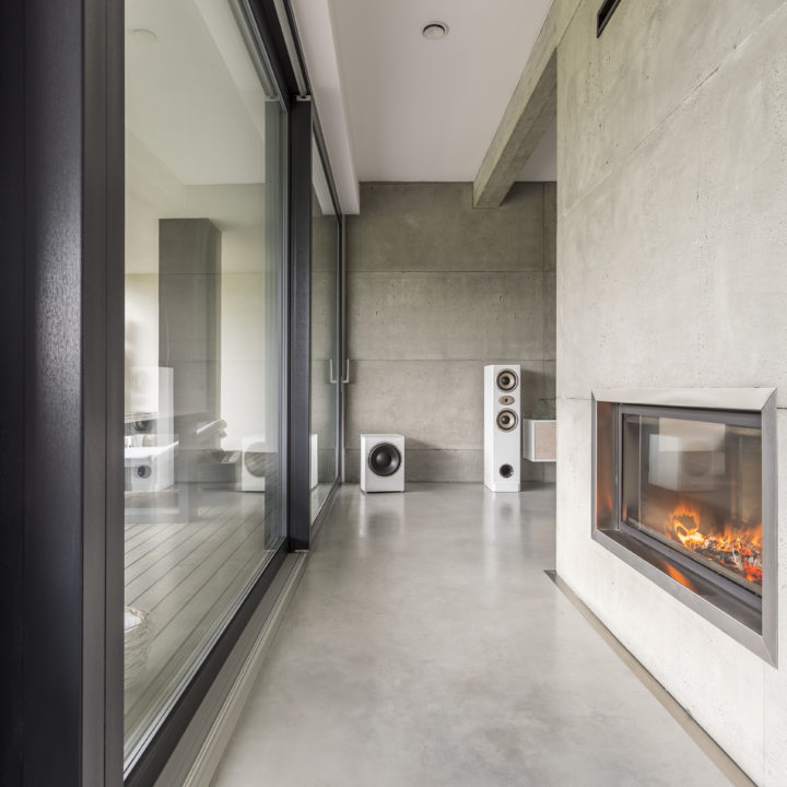 Fireplace on concrete wall in front of huge window in spacious apartment with loudspeakers